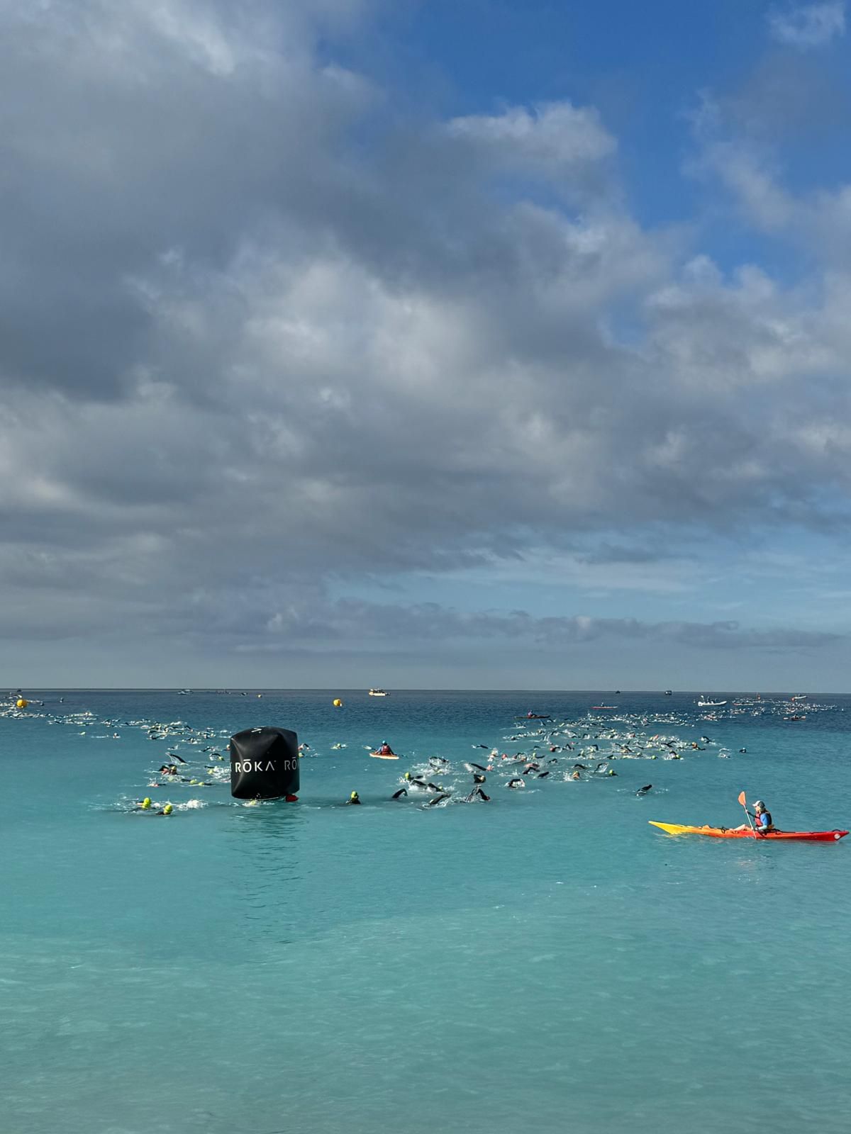 Départ de natation en eau libre : le peloton de nageurs autour d'une bouée, escorté par un kayak